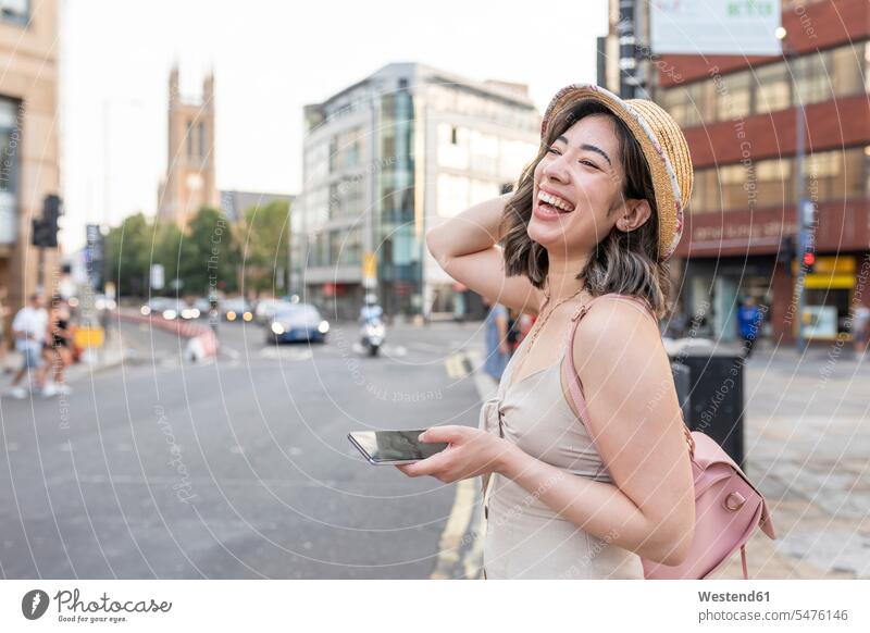 Frau, die lacht, während sie ein Smartphone auf der Straße in der Stadt benutzt Farbaufnahme Farbe Farbfoto Farbphoto Außenaufnahme außen draußen im Freien Tag
