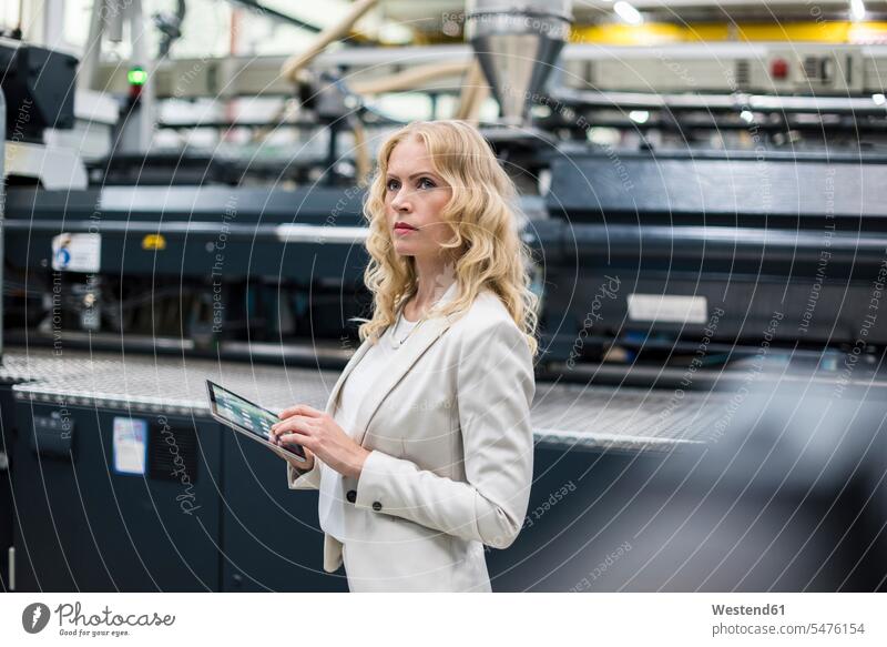 Frau mit Tablet an Maschine in Fabrikhalle schaut sich um Industriehallen Fabrikhallen weiblich Frauen Fabriken Maschinen umherblicken umschauen umsehen