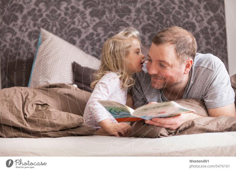 Vater und Tochter lesen im Bett ein Buch und flüstern sich ins Ohr Bücher Betten hoeren Lektüre reden Glück glücklich sein glücklichsein zufrieden liegend liegt