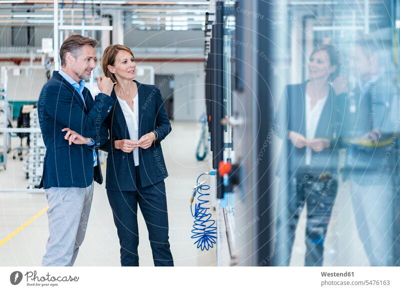 Geschäftsmann und Geschäftsfrau betrachten eine Maschine in einer modernen Fabrikhalle geschäftlich Geschäftsleben Geschäftswelt Geschäftsperson