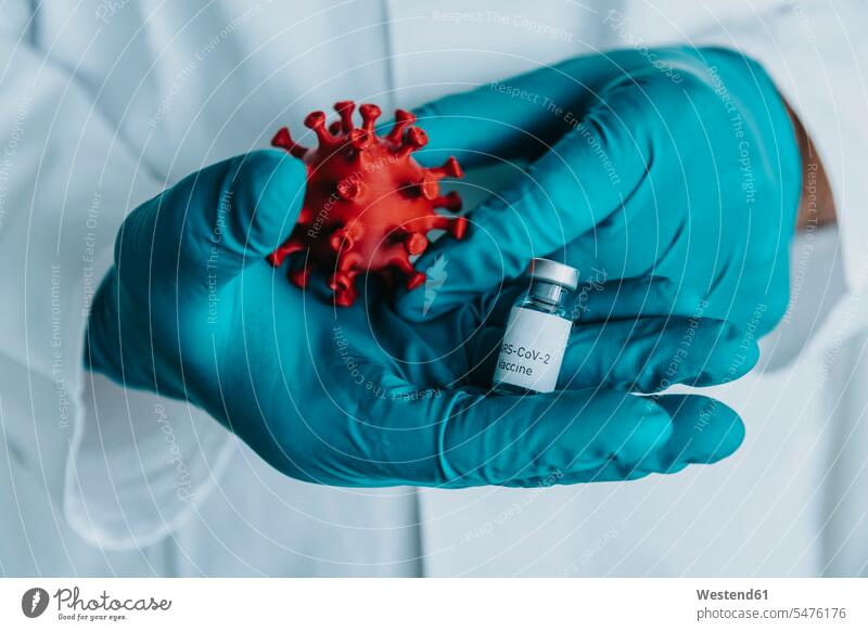 Nahaufnahme eines Wissenschaftlers, der eine Impfstoffflasche und ein Coronavirus-Modell in der Hand hält, während er im Labor steht Farbaufnahme Farbe Farbfoto