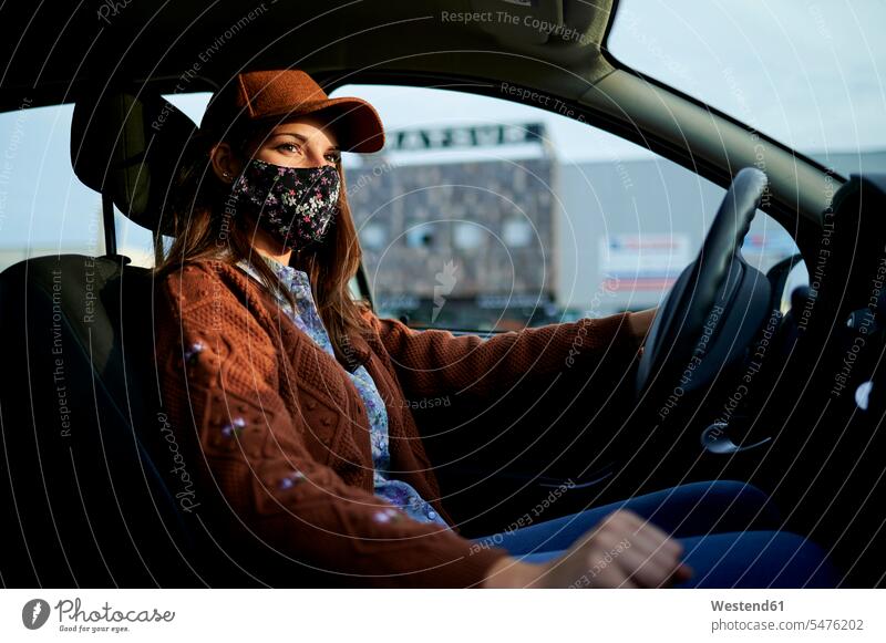 Junge Frau mit Mütze und Gesichtsmaske fährt Auto in der Stadt Farbaufnahme Farbe Farbfoto Farbphoto Tag Tageslichtaufnahme Tageslichtaufnahmen Tagesaufnahme