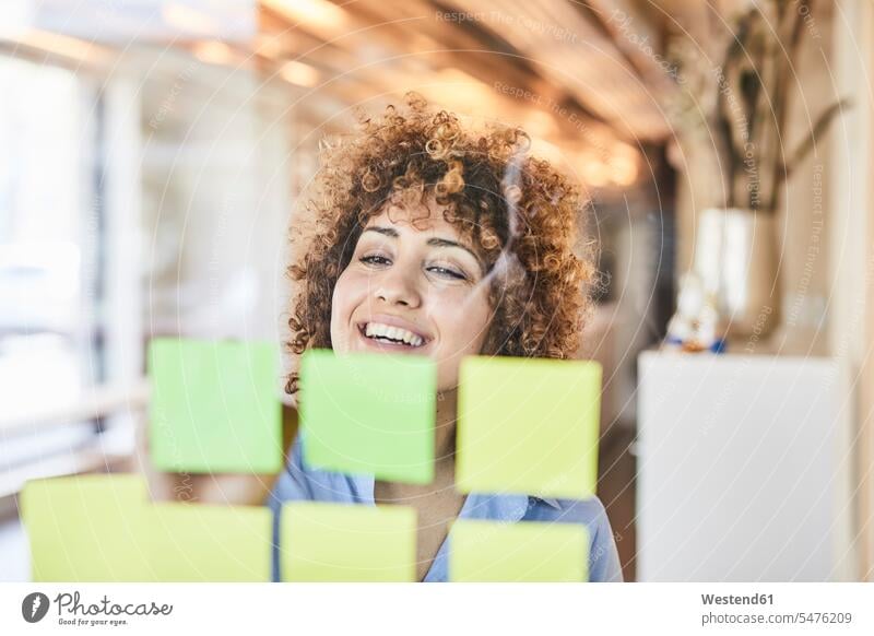 Glückliche Geschäftsfrau beim Brainstorming mit Post-its auf Glasscheibe lächeln Haftnotiz Haftnotizen Ideenfindung glücklich glücklich sein glücklichsein