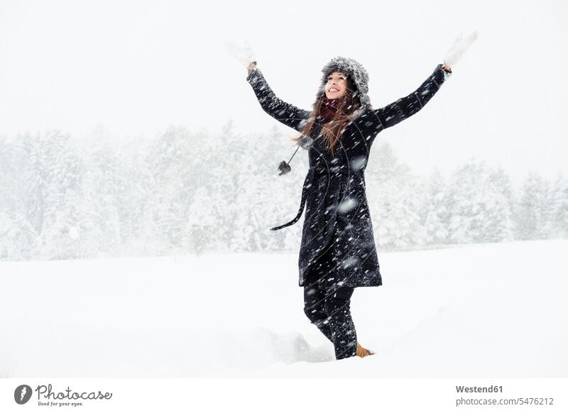 Porträt einer glücklichen jungen Frau, die in einer Winterlandschaft tanzt Handschuhe Mützen Jahreszeiten winterlich Winterzeit begeistert Enthusiasmus