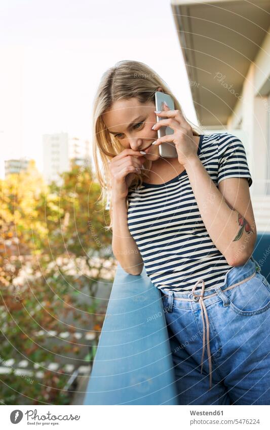 Lächelnde junge Frau, die auf dem Balkon mit dem Handy telefoniert Mobiltelefon Handies Handys Mobiltelefone Balkone lächeln telefonieren anrufen Anruf