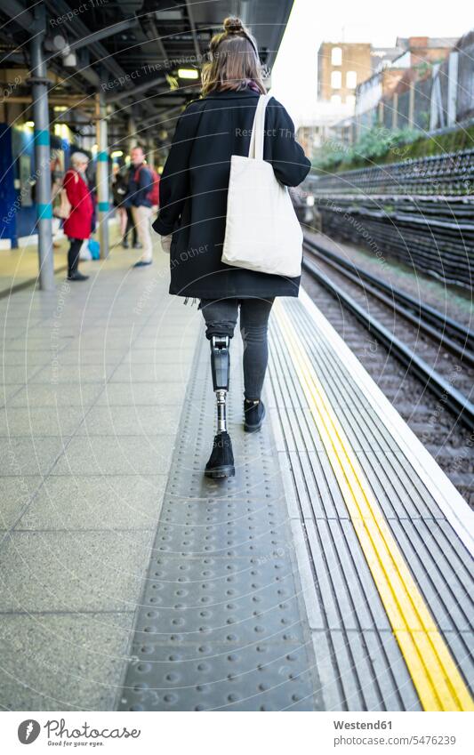 Rückansicht einer jungen Frau mit Beinprothese beim Gehen am Bahnsteig Leute Menschen People Person Personen Europäisch Kaukasier kaukasisch Nordeuropäisch 1