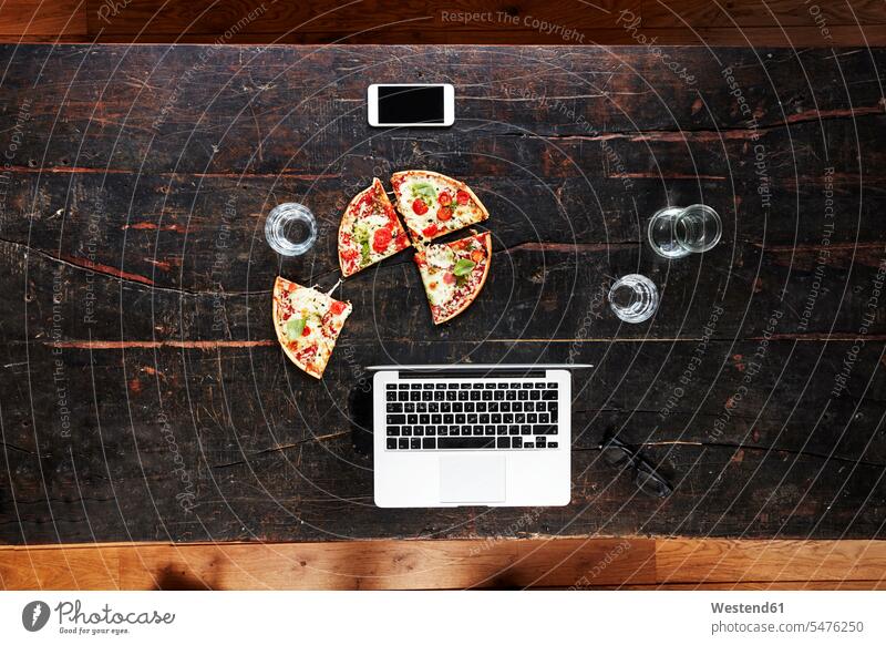 Laptop, Smartphone, Pizza und Wassergläser auf der Tischplatte, Draufsicht Holztisch Holztische Pizzen Wasserglas Wasserglaeser Fastfood Fast Food Freiberufler