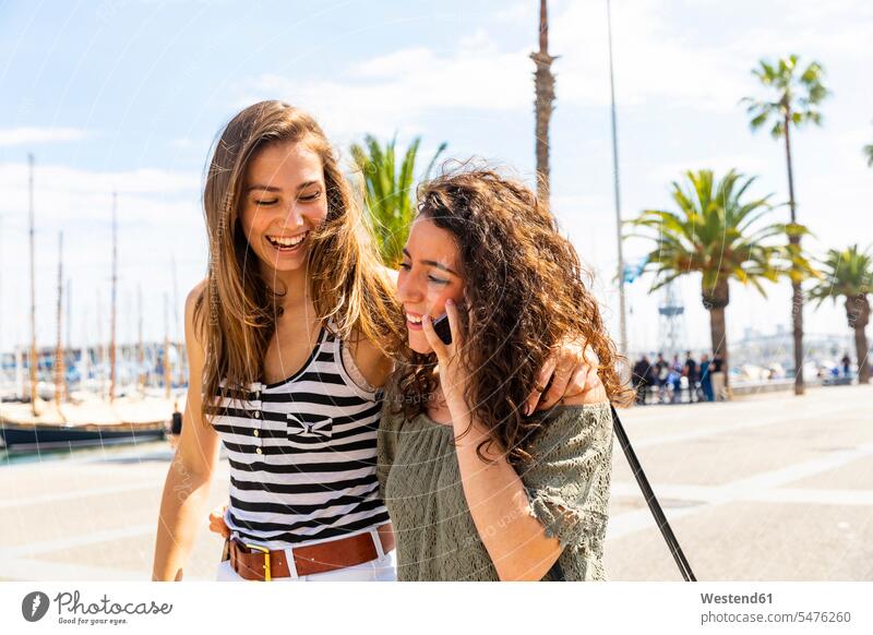 Zwei glückliche Freundinnen mit Handy an der Uferpromenade Glück glücklich sein glücklichsein Promenade Promenaden Mobiltelefon Handies Handys Mobiltelefone