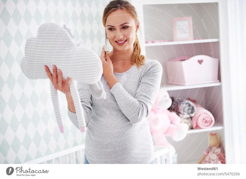 Schwangere Frau mit Kissen und Smartphone im Babyzimmer Erwartung erwartungsvoll erwarten Vorfreude Polster iPhone Smartphones betrachten betrachtend weiblich