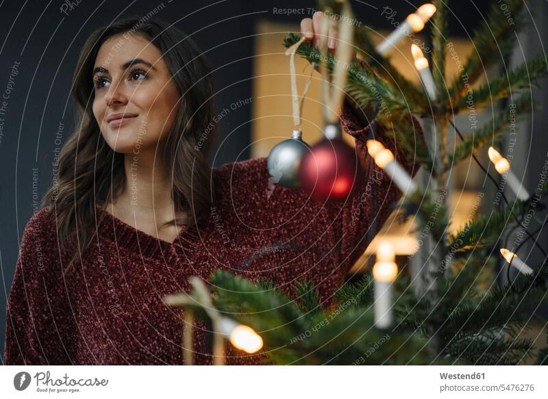 Junge Frau beim Schmücken des Weihnachtsbaums schaut weg Deutschland nachdenken überlegen Christbaumkugel Weihnachtskugeln Christbaumkugeln Vorfreude schmücken