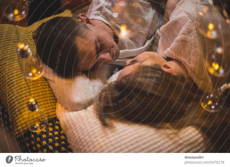 Romantisches junges Paar kuschelt im Bett mit Lichterketten Pärchen Paare Partnerschaft liegen liegend liegt kuscheln schmusen knuddeln romantisch schwärmerisch