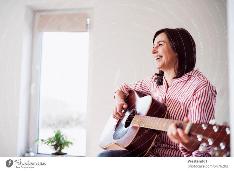 Glückliche reife Frau spielt Gitarre zu Hause braune Haare braunhaarig brünett braunes Haar Freizeitbeschäftigung Freizeitbeschaeftigung musizieren Musik machen