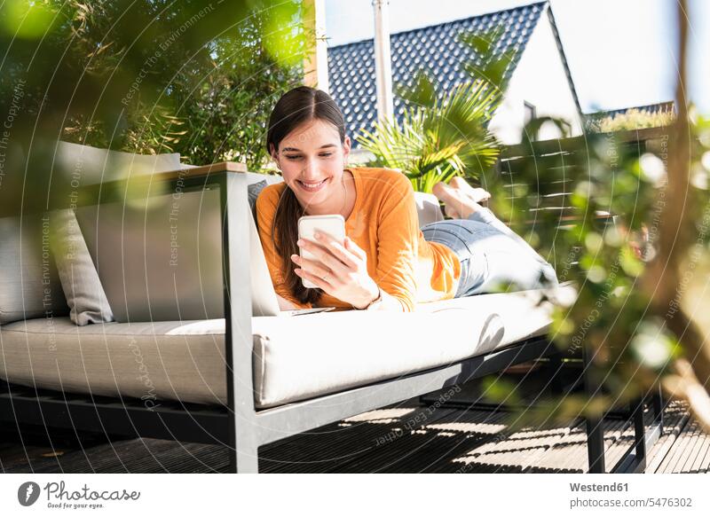 Junge Frau liegt auf der Couch auf der Terrasse mit Handy und Laptop eigenständig Eigenständigkeit selbstständig selbständig Selbständigkeit Spass spassig