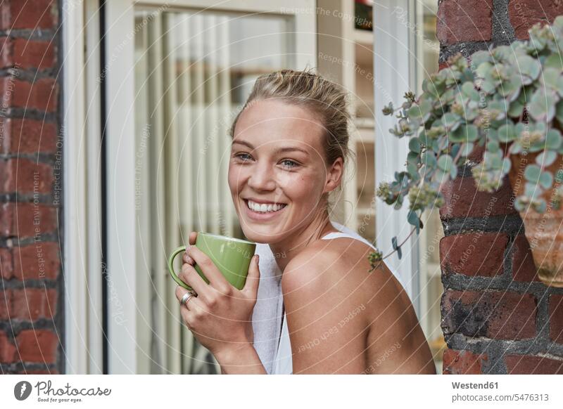 Porträt einer lächelnden sportlichen jungen Frau mit einer Tasse Kaffee am Hauseingang Kaffeetasse Kaffeetassen Portrait Porträts Portraits weiblich Frauen