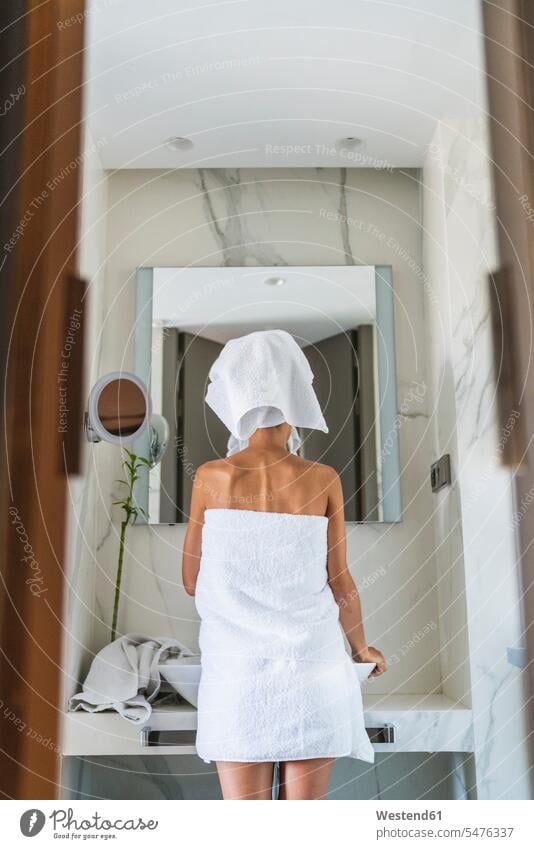 In Handtücher gewickelte Frau schaut in den Badezimmerspiegel In ein Handtuch gewickelt Turban weiblich Frauen Spiegel schauen sehend Erwachsener erwachsen