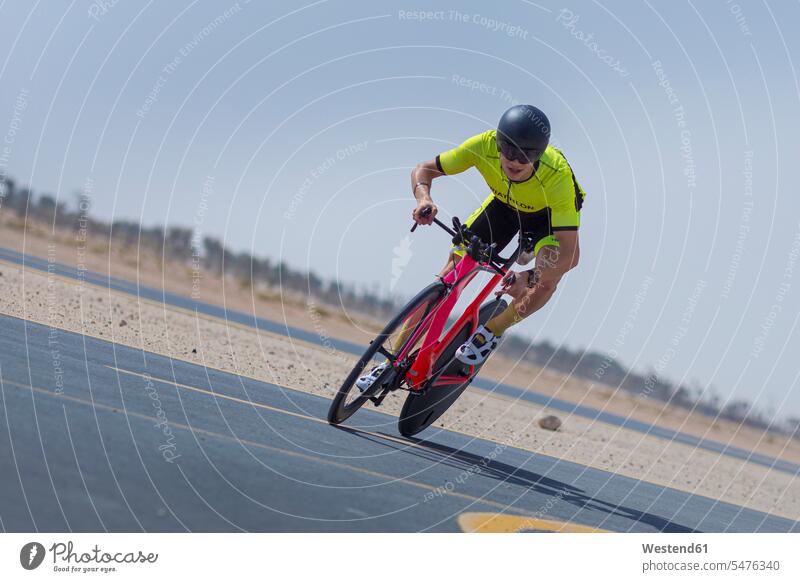 Entschlossener Radfahrer auf dem Fahrrad auf der Straße gegen den klaren blauen Himmel in der Wüste in Dubai, Vereinigte Arabische Emirate Farbaufnahme Farbe