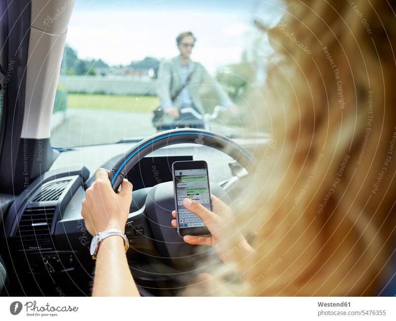 Junge Frau im Elektroauto simst mit dem Handy Auto Wagen PKWs Automobil Autos Mobiltelefon Handies Handys Mobiltelefone weiblich Frauen simsen Elektromobil