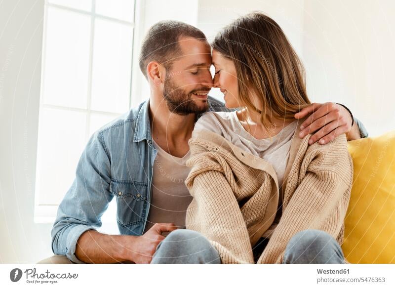 Zärtlich lächelndes Paar mit geschlossenen Augen in der Liebe zu Hause Polster knuddeln schmusen sitzend sitzt Arm umlegen Umarmung Umarmungen entspannen