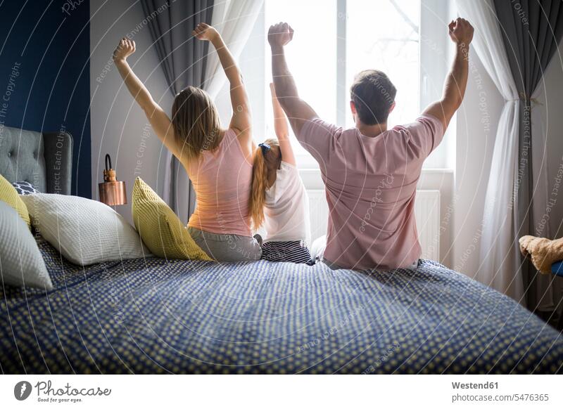 Glückliche Familie sitzt auf dem Bett, streckt sich, Rückansicht aufwachen erwachen Betten strecken dehnen Familien aufstehen erheben sitzen sitzend Mensch
