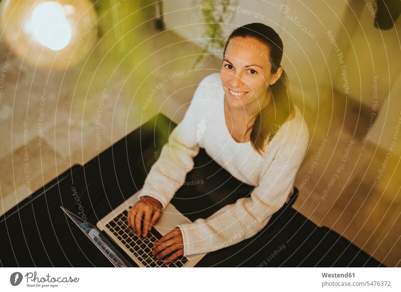 Lächelnde Frau sitzt mit Laptop auf der Kücheninsel Farbaufnahme Farbe Farbfoto Farbphoto Verbindung verbunden Anschluss verbinden Zuhause Häusliches Leben