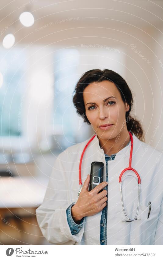Eine Ärztin steht in einem Hosptal und hält ein Telefon und ein Stethoskop in der Hand Leute Menschen People Person Personen Europäisch Kaukasier kaukasisch 1