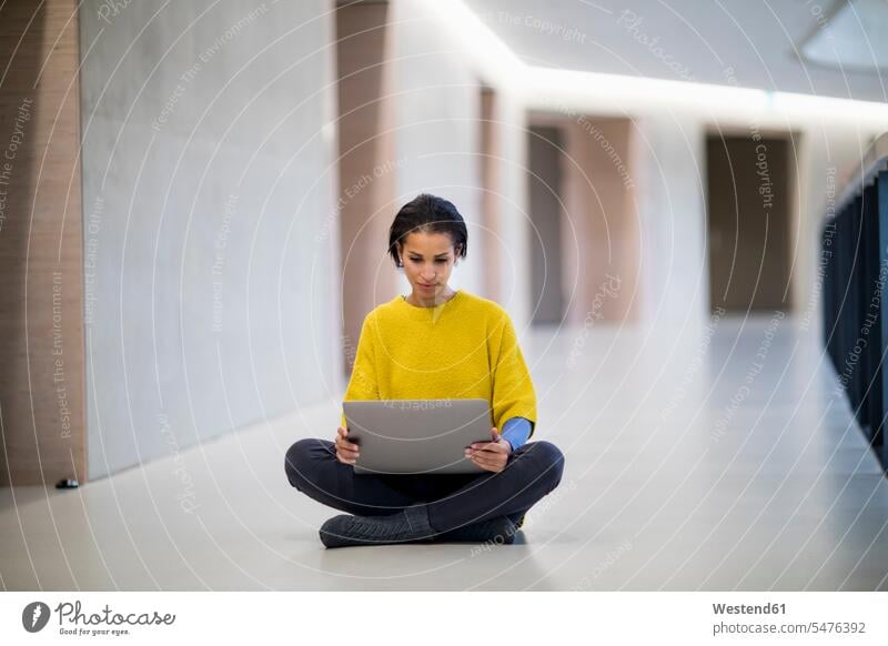 Porträt einer jungen Frau mit gelbem Pullover, die mit einem Laptop auf dem Boden sitzt Portrait benutzen Fußboden Erwachsener Mensch Farbe Computer