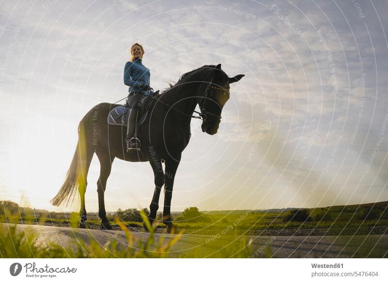 Frau zu Pferd auf einer Straße auf dem Land abends freuen geniessen Genuss Glück glücklich sein glücklichsein zufrieden Pferdesport Reitsport auf dem Lande frei