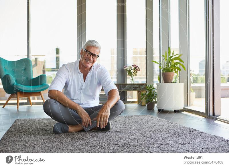 Porträt eines lächelnden reifen Mannes, der sich auf einem Teppich zu Hause entspannt Männer männlich Portrait Porträts Portraits entspanntheit relaxt sitzen