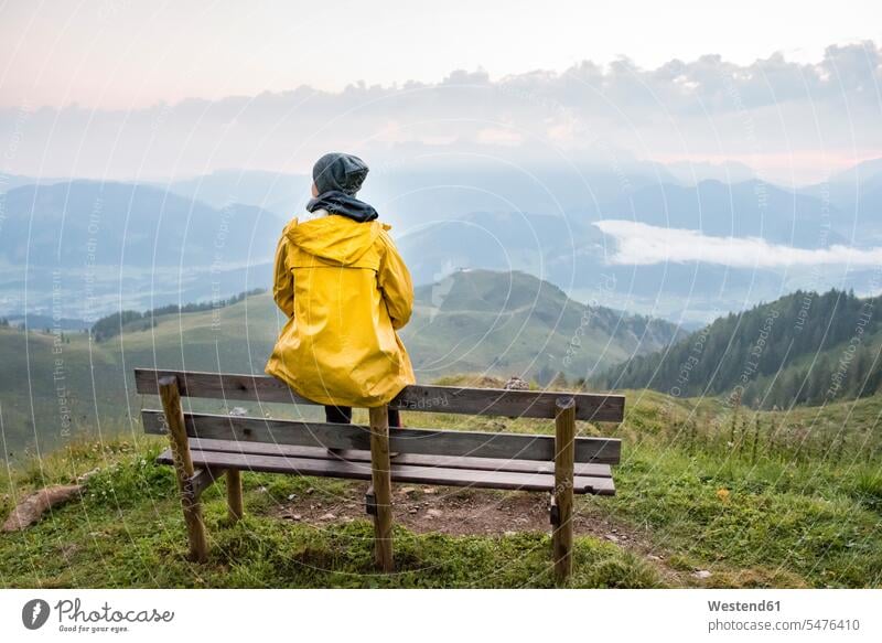 Österreich, Tirol, Fieberbrunn, Wildseeloder, Frau sitzt auf Bank mit Blick auf Berglandschaft Aussicht Ausblick Ansicht Überblick Sitzbänke Bänke Sitzbank