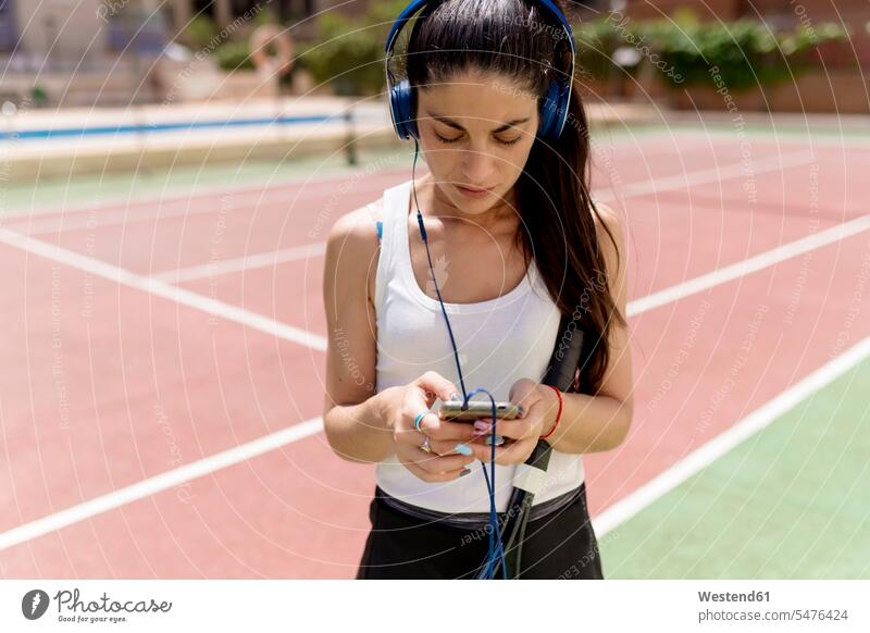 Tennisspielerin benutzt Smartphone, während sie an einem sonnigen Tag auf dem Tennisplatz Musik hört Farbaufnahme Farbe Farbfoto Farbphoto Spanien Außenaufnahme