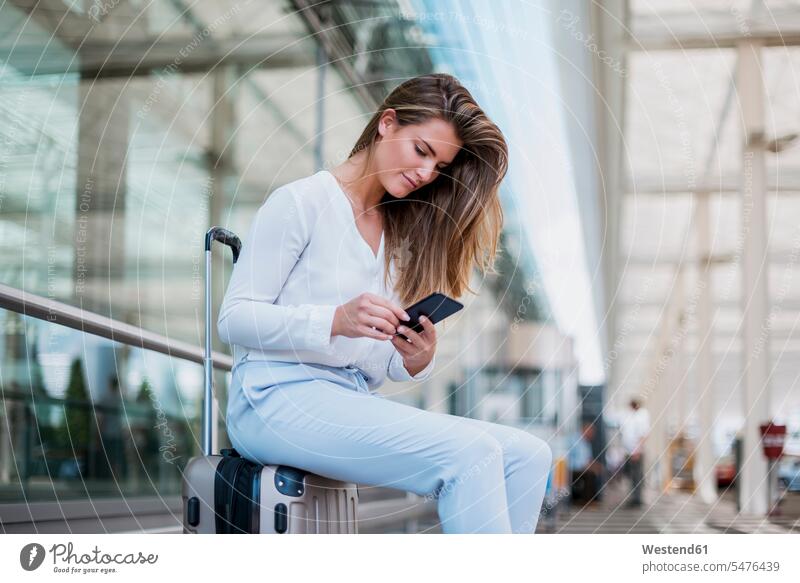 Junge Geschäftsfrau sitzt mit ihrem Handy im Gepäck im Freien Koffer sitzen sitzend Reisegepäck Mobiltelefon Handies Handys Mobiltelefone Geschäftsfrauen