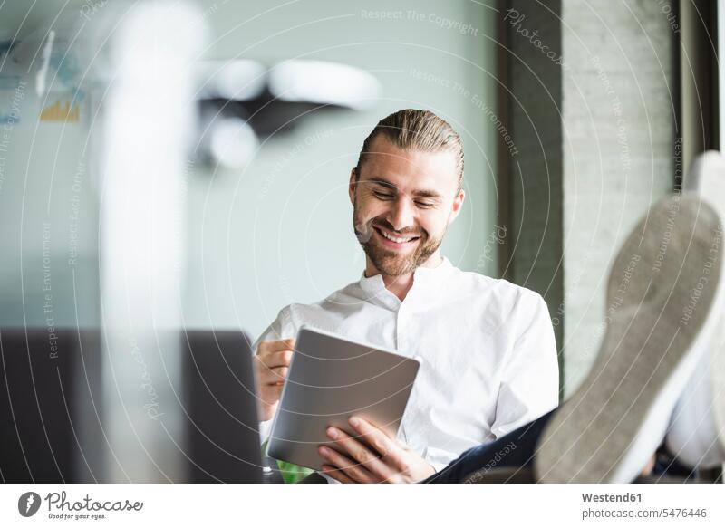 Lächelnde Geschäftsmann sitzt im Büro mit Füßen oben mit Tablette lächeln Office Büros Tablet Computer Tablet-PC Tablet PC iPad Tablet-Computer sitzen sitzend