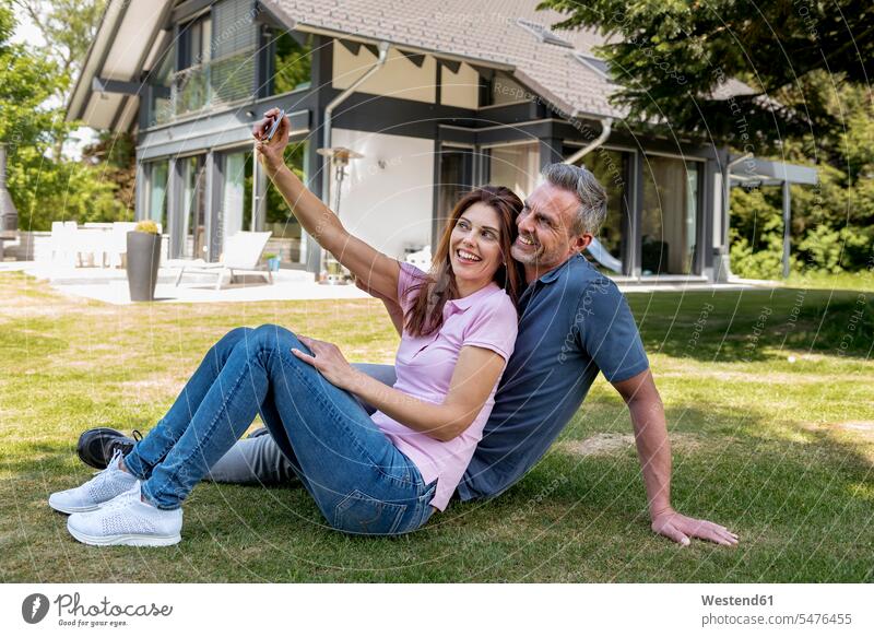 Glückliches Paar sitzt im Garten seines Hauses und macht ein Selfie glücklich glücklich sein glücklichsein Häuser Haeuser Selfies Gärten Gaerten Pärchen Paare