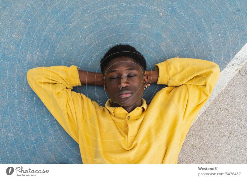Junger schwarzer Mann schlafend auf dem Boden, mit Händen hinter dem Kopf Schwarzer Afrikanisch Farbige Afrikanische Abstammung dunkelhäutig Farbiger Portrait