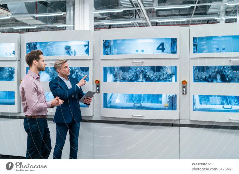 Zwei Geschäftsleute mit Tablettsprechen an der Maschine in einer modernen Fabrik Arbeitskollege Arbeitskollegen Kollege Partner Partnerschaften Job Berufe