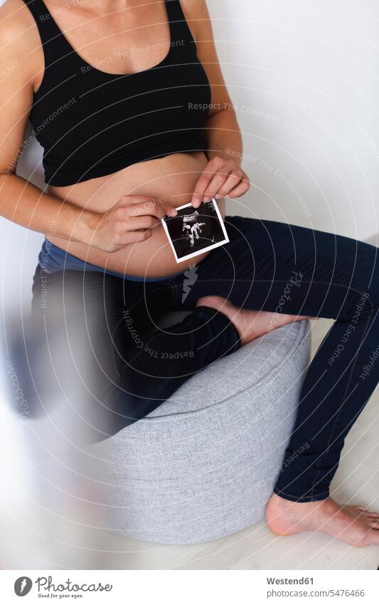 Junge schwangere Frau mit Ultraschallbild ihres ungeborenen Babys Oberkoerper Oberkörper Torso Torsos Bäuche sitzend sitzt Glück glücklich sein glücklichsein