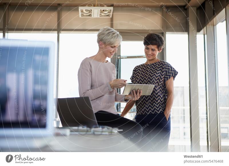 Zwei lächelnde Geschäftsfrauen teilen sich ein Tablet im Büro Teilen Sharing arbeiten Arbeit Office Büros Businesswomen Businessfrauen Businesswoman Kollegin