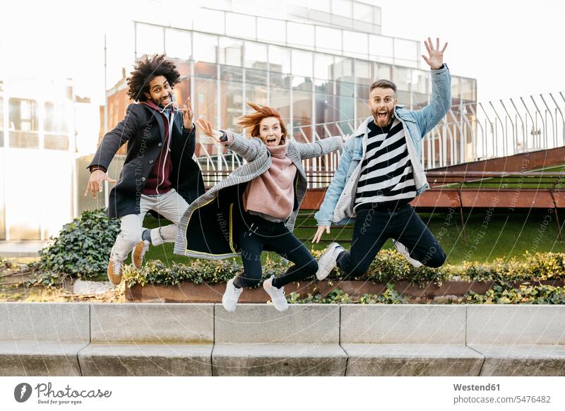 Drei glückliche Freunde springen in der Stadt staedtisch städtisch Glück glücklich sein glücklichsein hüpfen Freundschaft Kameradschaft Außenaufnahme draußen