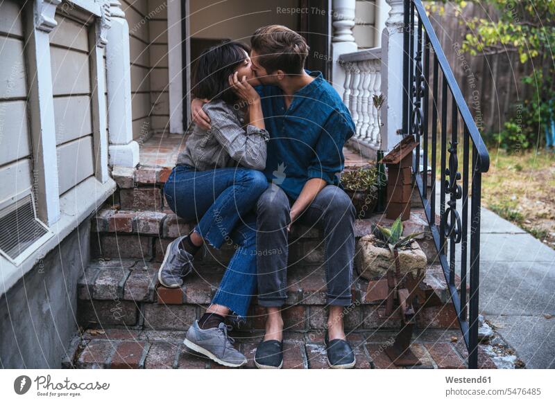 Auf gebückter Haltung sitzendes Paar küsst sich sitzt Pärchen Paare Partnerschaft küssen Küsse Kuss Hauseingang Eingangsterrasse Mensch Menschen Leute People