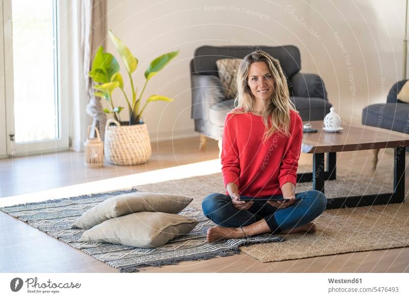 Porträt der lächelnden Frau sitzt auf dem Boden zu Hause hält Tablette Zuhause daheim Böden Boeden sitzen sitzend weiblich Frauen Tablet Computer Tablet-PC