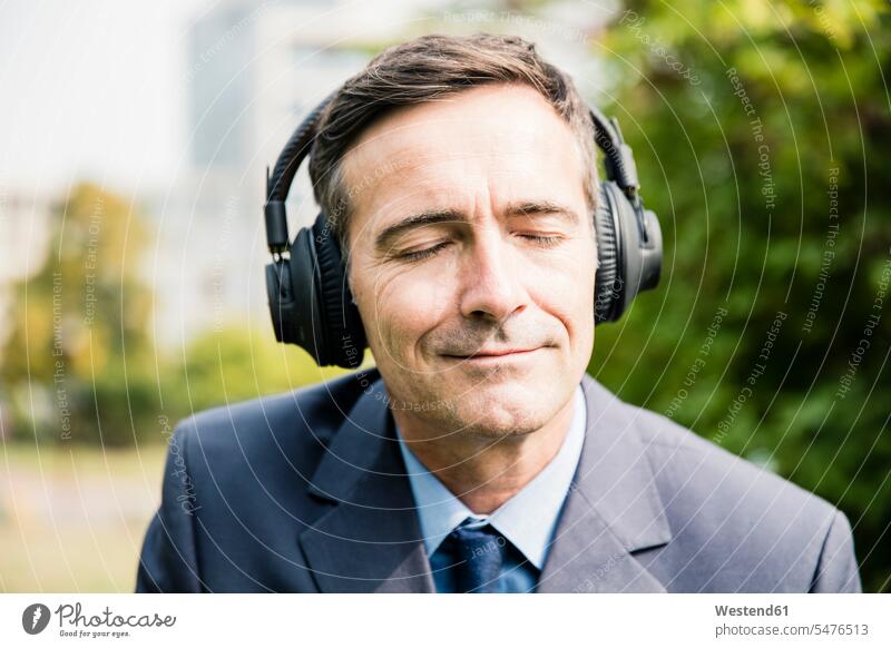 Geschäftsmann mit geschlossenen Augen, der mit Kopfhörern Musik hört hören hoeren Businessmann Businessmänner Geschäftsmänner Kopfhoerer Geschäftsleute