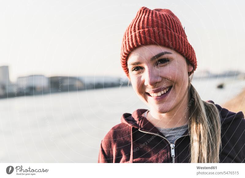 Porträt einer lächelnden, sportlichen jungen Frau am Flussufer in der Stadt Fluesse Fluß Flüsse staedtisch städtisch Portrait Porträts Portraits weiblich Frauen