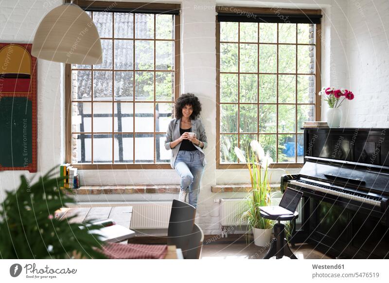 Frau steht am Fenster ihrer Loft-Wohnung und trinkt Kaffee Lofts stehen stehend weiblich Frauen Zuhause zu Hause daheim trinken Klavier Piano Pianos Klaviere