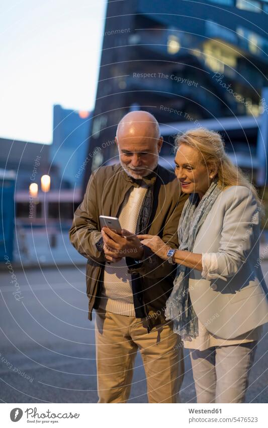 Spanien, Barcelona, älteres Paar teilen Handy in der Stadt in der Abenddämmerung Teilen Sharing Mobiltelefon Handies Handys Mobiltelefone stimmungsvoll Stimmung