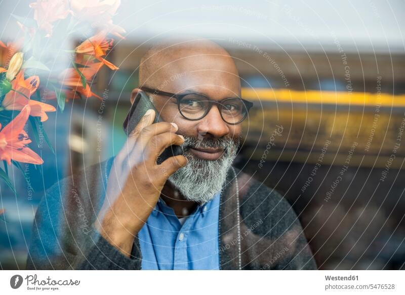 Porträt eines lächelnden Mannes am Telefon hinter einer Fensterscheibe Portrait Porträts Portraits telefonieren anrufen Anruf telephonieren Fensterscheiben