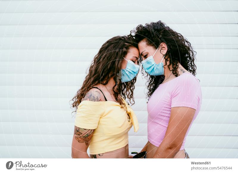 Lesbisches Paar mit Masken, das mit dem Gesicht gegen die Wand in der Stadt steht Farbaufnahme Farbe Farbfoto Farbphoto Spanien Freizeitbeschäftigung Muße Zeit