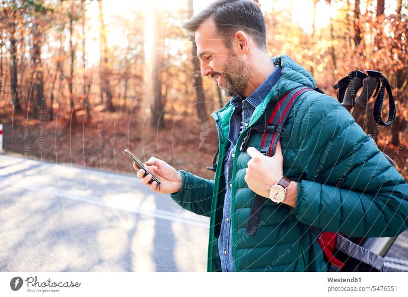 Lächelnd Mann Überprüfung Smartphone auf einer Straße in den Wäldern während Rucksacktour iPhone Smartphones Rucksäcke checken Strassen Straßen lächeln Männer