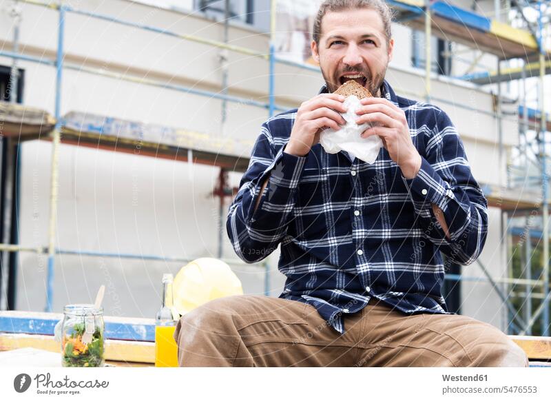 Bauarbeiter isst Brot, während er auf der Baustelle gegen das Gebäude sitzt Farbaufnahme Farbe Farbfoto Farbphoto Deutschland Architektur Baukunst Baustellen