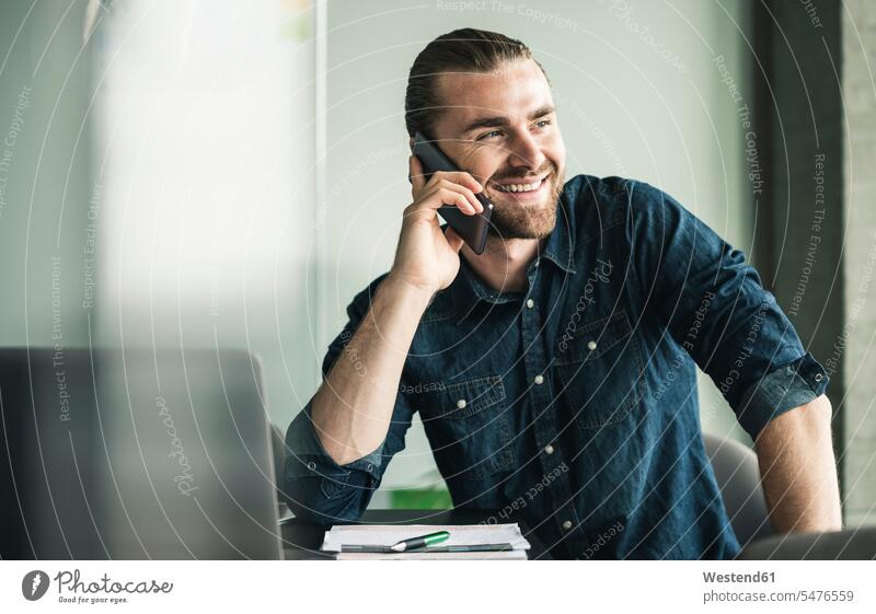 Lächelnder junger Geschäftsmann am Handy im Büro lächeln Businessmann Businessmänner Geschäftsmänner Office Büros Mobiltelefon Handies Handys Mobiltelefone