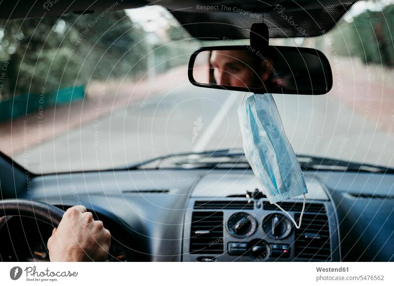 Nahaufnahme einer schützenden Gesichtsmaske, die am Rückspiegel im Auto  hängt - ein lizenzfreies Stock Foto von Photocase